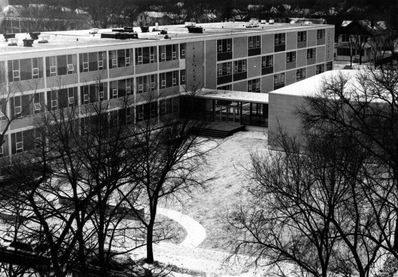 A multi‑story modern building seen from above, with leafless trees and a snow‑covered courtyard in front.