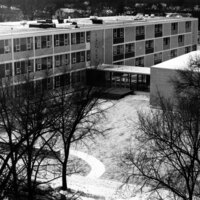 A multi‑story modern building seen from above, with leafless trees and a snow‑covered courtyard in front.